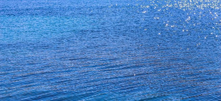 Blue sea in sunshine glow as surface background. Summer holidays and coastal nature concept