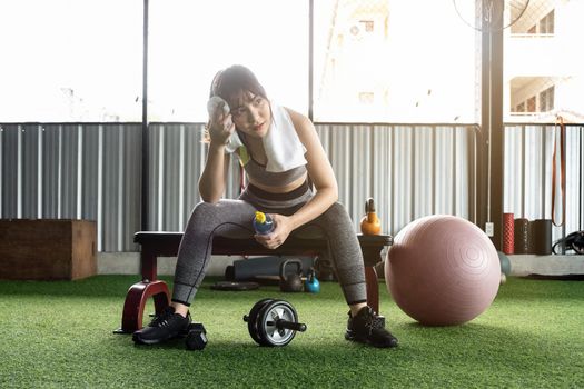 Attractive fitness woman sitting on a chair and resting after workout at fitness centre. Female take a break after hard cardio.