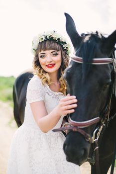 girl with red lips in a white dress near a black horse