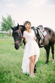 girl with red lips in a white dress near a black horse