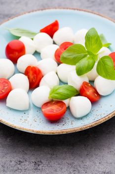 Cherry tomatoes, mozzarella cheese, basil and spices on gray slate stone chalkboard. Italian traditional caprese salad ingredients. Mediterranean food.