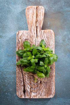 Bunch of fresh organic basil in cutting board on rustic wooden background