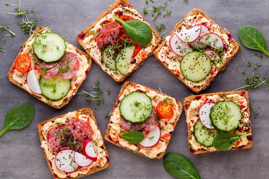 Sandwiches with cream cheese, vegetables and salami. Sandwiches with cucumber, radish, tomatoes, salami on a gray background, top view. Flat lay.