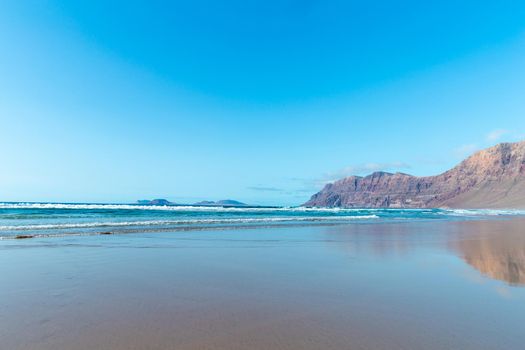 Panorama of beautiful beach and tropical sea of Lanzarote. Canaries. Coast of Famara beach, Lanzarote Island, Canary Islands. Tourists on the most popular beach at the island of Lanzarote.