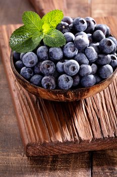 Bowl of fresh blueberries on rustic wooden board. Organic food blueberries and mint leaf for healthy lifestyle.