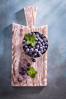 Bowl of fresh blueberries on rustic wooden board. Organic food blueberries and mint leaf for healthy lifestyle.