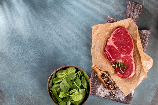 Fresh raw rib-eye steak on wooden cutting board, with spinach, lentils and rosmary in a rustic style.