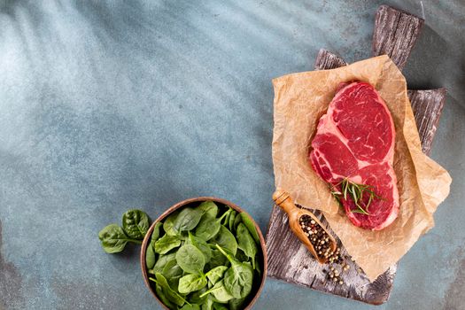 Fresh raw rib-eye steak on wooden cutting board, with spinach, lentils and rosmary in a rustic style.