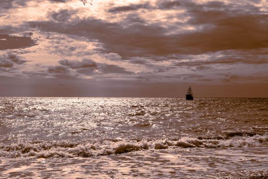 Seascape. A sailing ship sails across the sparkling sea against the background of a dark sky, golden toning. Sea travel