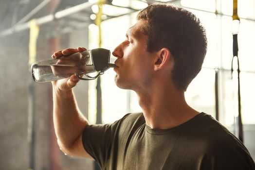 So thirsty. Young athletic man drinking water while exercising at gym. Healthy lifestyle. Professional sport. TRX Training.