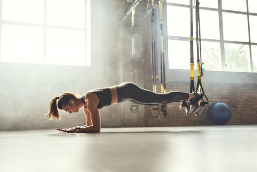 Healthy lifestyle. Young athletic woman doing plank with trx fitness straps in the gym. Professional sport. TRX Training. Workout