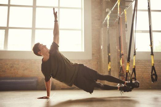 Making perfect body. Young athletic man exercising with suspension straps at gym. TRX Training. Fitness concept. Active life