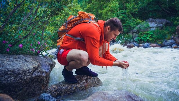 Man tourist sitting on rocks near mountain river and refreshing himself.