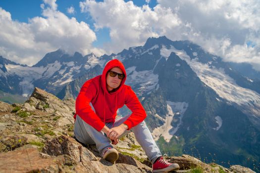 Adult male in red hoodie with hood enjoying beautiful view in mountainous area.