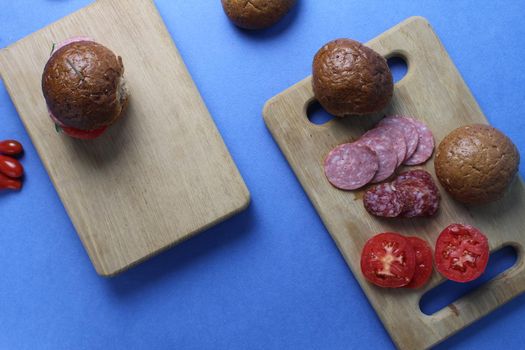 food layout buckwheat buns vegetables sausage tomato onion lie on a wooden tray on a blue bright background. Top view. Products for making sandwich burgers homemade fast food.