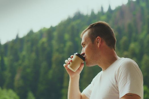 Adult male enjoying hot drink against mountain landscape.