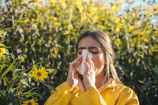 Woman with napkin fighting blossom allergie outdoor. Portrait of an allergic girl surrounded by seasonal flowers in bright yellow color. Beautiful girl having an allergic reaction to flowers