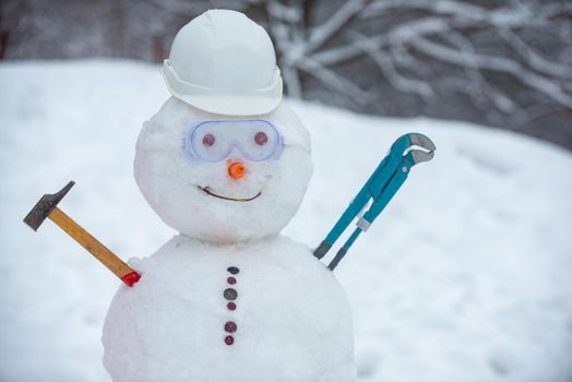 Snowman worker on snow background. Funny snowman in work helmet on snowy field. Handmade snowman in the snow outdoor