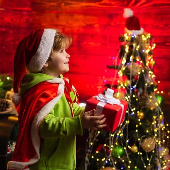 Merry christmas and happy new year. Little boy with Christmas presents. Pretty toddler boy in Christmas Santa hat holds a gift box and beautiful luxury decorated background