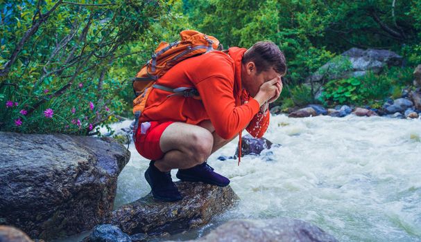 Man tourist sitting on rocks near mountain river and refreshing himself.