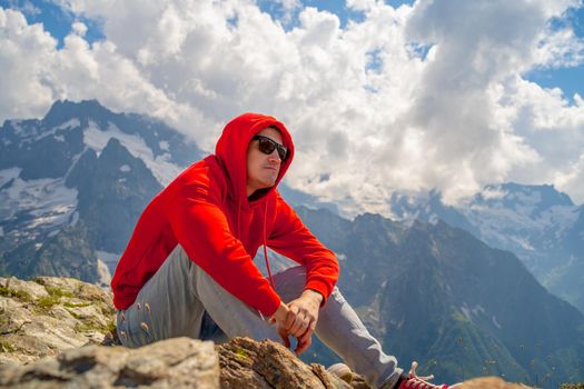 Adult male in red hoodie with hood enjoying beautiful view in mountainous area.