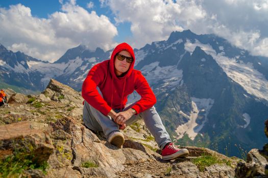 Adult male in red hoodie with hood enjoying beautiful view in mountainous area