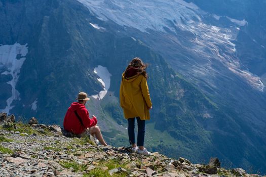 Male sitting on rock and female standing, they looking at mountain landscape.