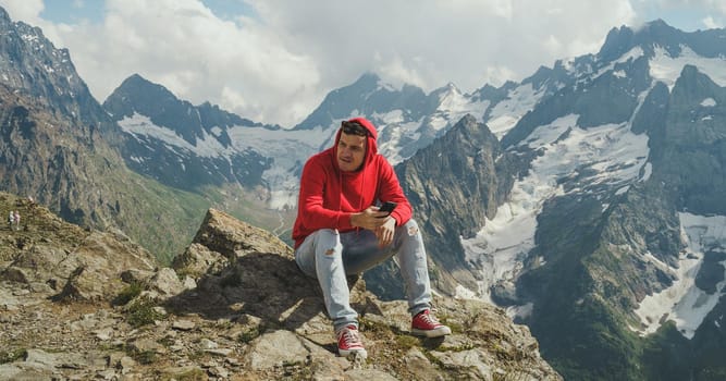 Male traveler using mobile phone against cloudy sky on sunny day in mountainous terrain.