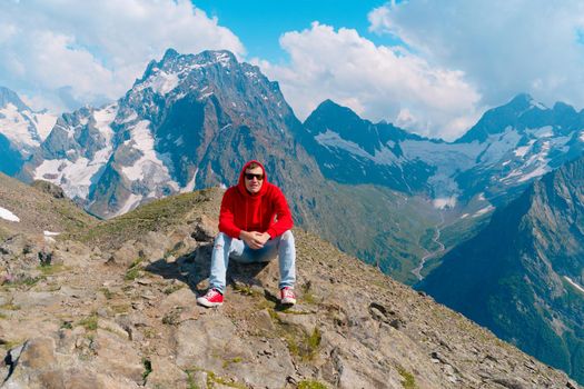 Adult male in red hoodie with hood enjoying beautiful view in mountainous area.