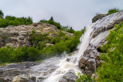 Rapid water stream falling from rocks against blue sky on sunny summer day in countryside