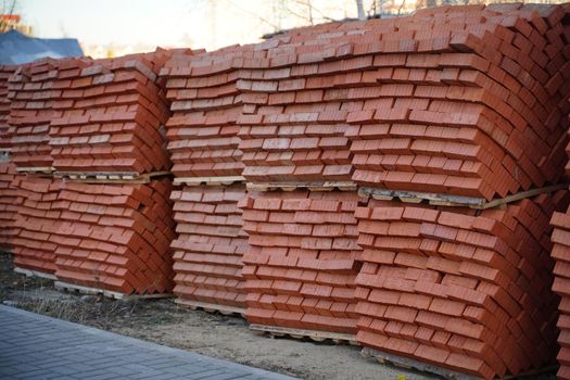 Pile of pallets with red bricks on city street. Building materials on construction site outdoor. Concept of constructing buildings