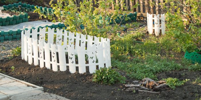 A white plastic fence around a flower bed. Garden decoration in early spring.