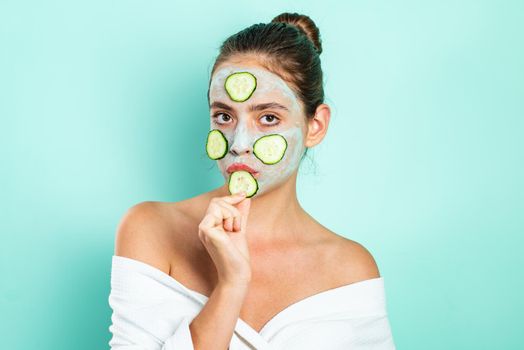 Sexy young girl with a mask for skin and slices of cucumbers on face. Happy mood and selfcare. Natural beauty concept. Beautiful woman with off shoulders eats a cucumber