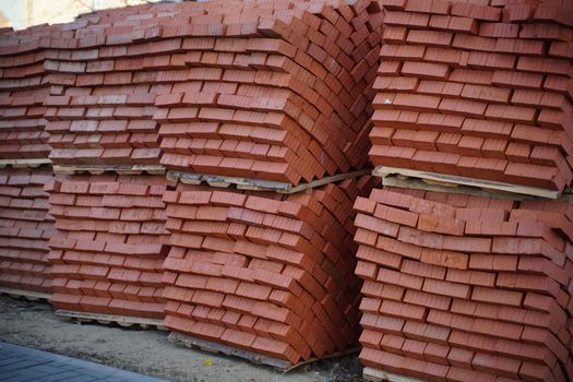 Pile of pallets with red bricks on city street. Building materials on construction site outdoor. Concept of constructing buildings