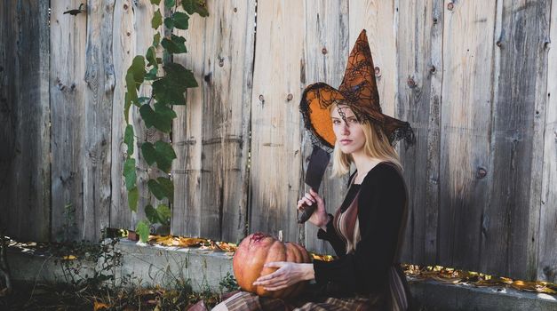 Halloween Witch. Witch posing with Pumpkin wearing black hat. Crazy Halloween. Happy gothic young woman in witch halloween costume. Halloween concept