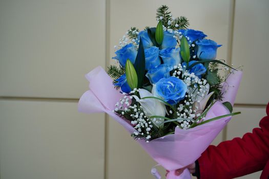 Close up of woman's hand holds colorful bouquet of flowers. Unrecognizable female holding flower composition of blue roses and white lilies in wrapping paper