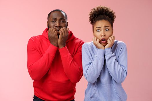 Shocked scared two insecure young african american couple both frightened spiders standing bed terrified freeze from fear holding hands mouth biting fingers shaking horror, pink background.