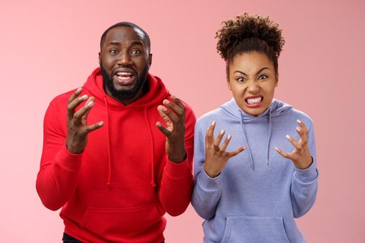 Two siblings upset failure losing bet watching football match cringing sorrow reckless, raising hands dismay sadness express regret anger being disappointed, standing pink background distressed.