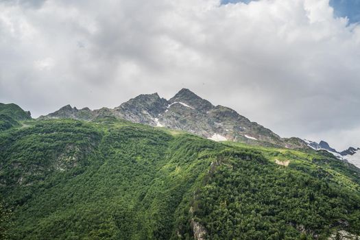 Mighty mountains with snow and green array in cloudy weather.