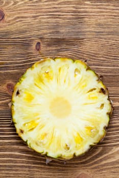 cut across a yellow fresh pineapple, which lies on a wooden board, closeup
