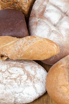 fresh loaves of different kinds of wheat and rye bread on a wooden surface, closeup