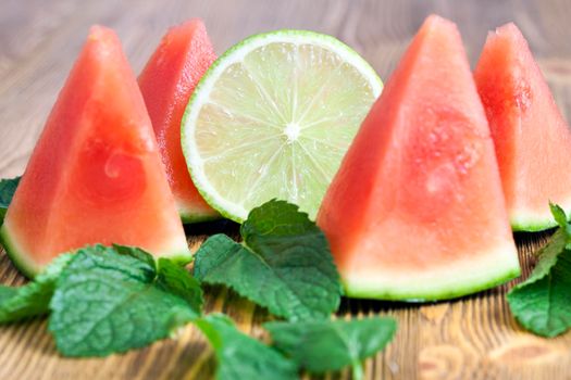 pink watermelon slices together with mint leaves and lime slice on the table