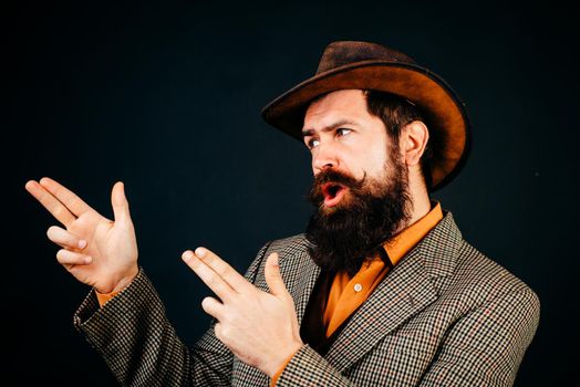 Bearded cowboy in suit and hat isolated at black background. Hipster self confident man wearing retro style suit and hat. Cool bearded gesticulative man