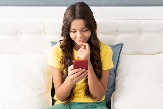 Happy girl child smile chatting on mobile phone while sitting on bed, chat.