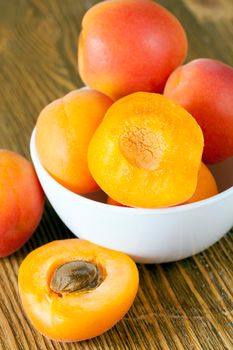 fresh washed apricots lying in a white bowl and some cut into halves, closeup of an appetizing meal of fruits