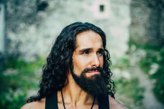 Sad frustrated man with long dark wavy hair and beard looking far away. Portrait of handsome man with disappointed face. Middle-aged sexy man with long hairstyle