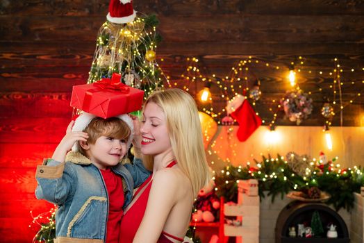 Smiling blonde femme dance with little boy. Portrait of happy positive woman holding kid against wooden background in the decorated room. Happy family couple