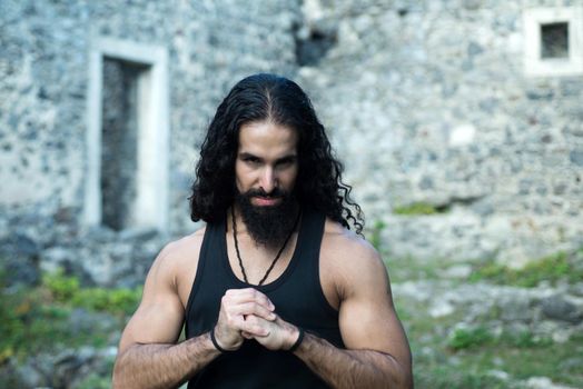 Strong confident man with long wavy dark hair and beard looking at camera. Young stylish man with determined character. Mans power and confidence concept