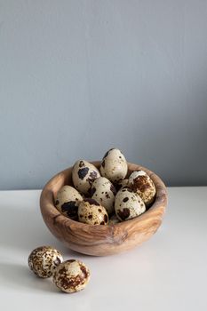 Speckled quail eggs in a wood bowl on a farm table in the kitchen.