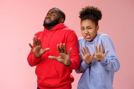 Studio shot pair african american friends woman man cringing disgust dislike feel awkward reluctant step back raise palms defensive refusing rejecting try stinky product, standing pink background.